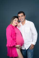 Happy Caucasian pregnant couple standing side-by-side against a dark blue background