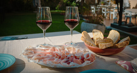 Table set for an aperitif. Two glasses of red wine and raw ham. Italian appetizer.
