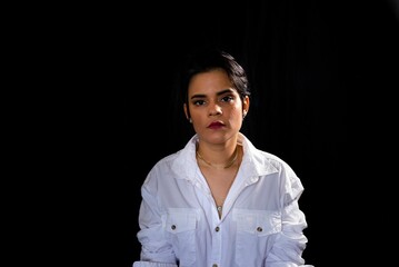 Young woman with a severe expression wearing a white outfit poses on a black background