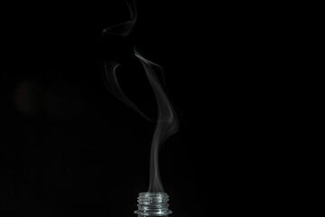 Plastic bottle with its lid off emits a plume of smoke into the air on the dark background