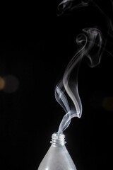 Plastic bottle with its lid off emits a plume of smoke into the air on the dark background