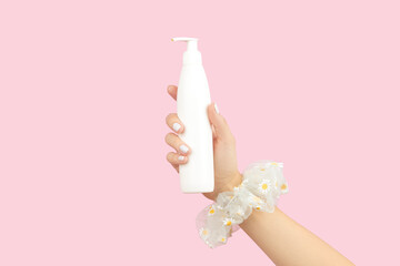 Womans hand holding white tube on pastel pink background. Self care beauty treatment concept