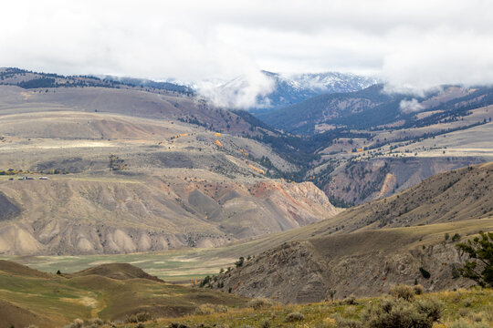 View of a valley from the top of a mountain in Yellowstone national park, images shows the low ground and steep cliffs with a snow covered mountain in the background