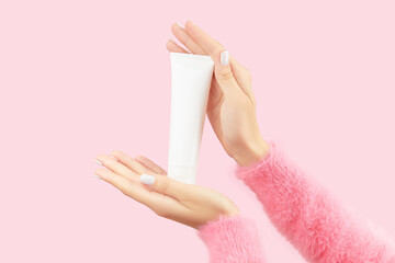 Womans hands holding white tube on pastel pink background. Self care beauty treatment concept