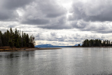 Snow covered mountains across lake yellowstone, Image shows a beautiful calm lake in Yellowstone national park on a cloudy day with a mountain and forest background