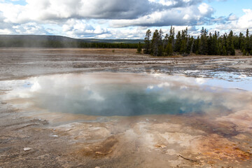 View of the multicolored Opal Pool in Yellowstone National Park with blue cloudy skies on a cold...