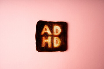 slice of dark burnt charred white bread with word ADHD on it on pink background. Conceptual image...