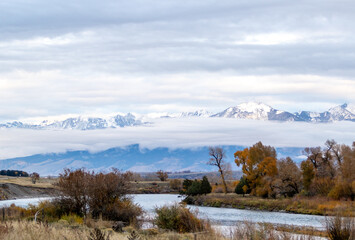 Obraz premium River view with low level cloud and snow covered mountains on the outskirts of Yellowstone national park on a cold autumn's day