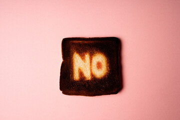 burnt slice of white bread toast with the word No on it on pink  background passionate ardent disagreement. poster creative rejection concept composition  - obrazy, fototapety, plakaty