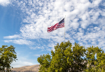 American flag waving on a windy day along the Columbia river on a beautiful sunny day with light cloud and a bush 