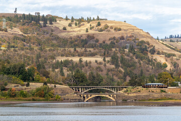 Naklejka premium Two bridges over the Columbia river, Image shows a bridge on a calm river reflecting the landscape off the water and steep hills with cloud and blue sky in the background