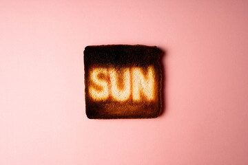 dark burnt slices of white bread toast with the word Sun on it on pink background. passionate Sunbathing. creative concept composition representation danger of sun radiation and photo aging