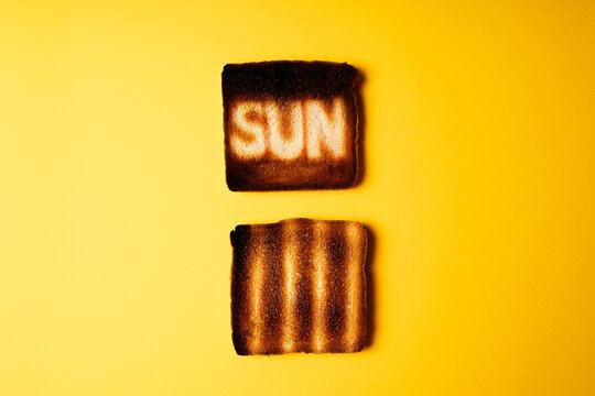 yellow poster with two burnt slices of white bread toast with the word Sun on it.  passionate ardent hot sun lovers. creative concept composition representation danger of sun radiation and photo aging