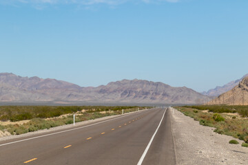 endless road in the desert, route 93, image shows a endless asphalt road in the Nevada desert, surrounded by untouched land and sand, with distant mountain views and rocks, taken october 2023