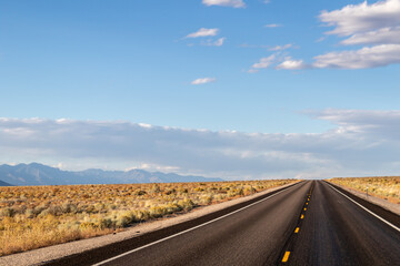 endless road in the desert, route 93, image shows a endless asphalt road in the Nevada desert, surrounded by untouched land and sand, with distant mountain views and rocks, taken october 2023