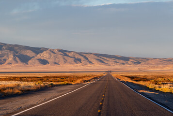 sunset in the desert, image shows the beautiful golden sunset glow in the Nevada desert with some clouds, a empty long asphalt road and a mountain view in the background, taken october 2023