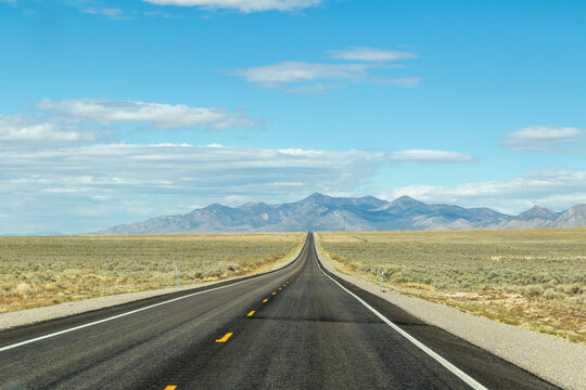 endless road in the desert, route 93, image shows a endless asphalt road in the Nevada desert, surrounded by untouched land and sand, with distant mountain views and rocks, taken october 2023