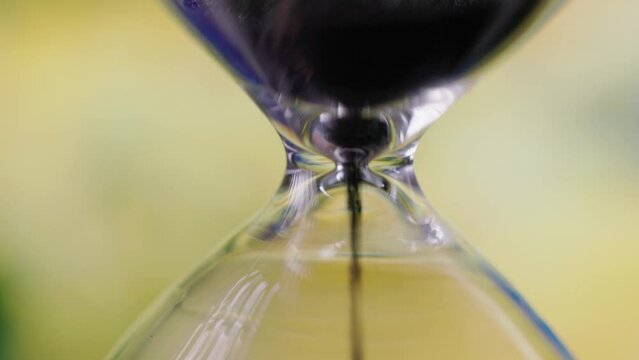 Closeup of the black sand pouring in the hourglass on the yellow background