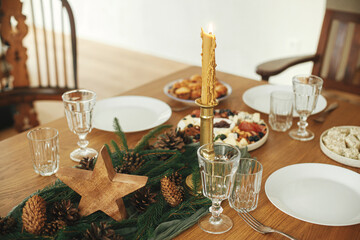 Christmas table setting. Stylish table runner with fir branches and pine cones, candles, cheese...