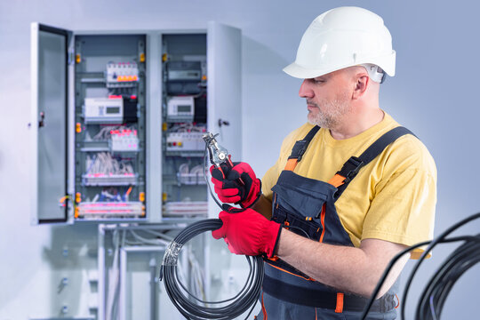 Man Electrician With Wire. Electrical Panel. Electrical Installation Work Inside Building. Electrician Cuts Power Cable. Man From Energy Company. Electrician At Work. Engineer Installs Grounding