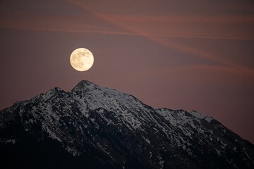 Beautiful full moon setting over majestic snow covered mountains.