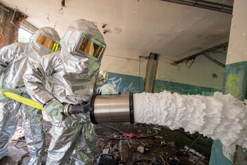 Firefighters in special protective suits against heat spray extinguishing foam used to extinguish...