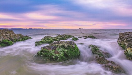 Long exposure shot of a tranquil sea with rocky shores at sunset.