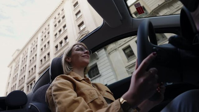 Confident young adult Caucasian woman enjoys driving an electric convertible vehicle in city, embodying freedom and eco-friendly living.  Eco-conscious woman enjoys a ride in sustainable electric auto