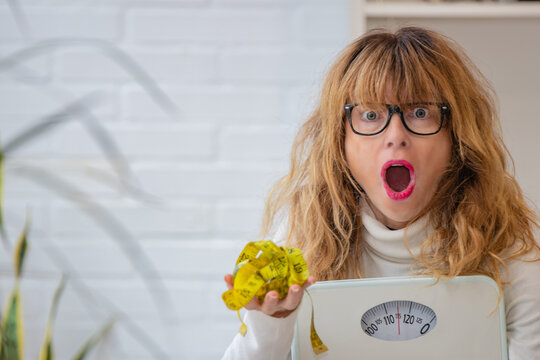 middle aged woman with scale looking at the measuring tape with expression of surprise