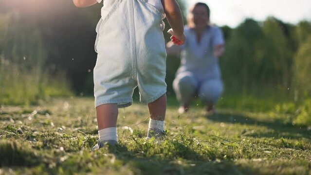 First steps. Childhood dream concept. Happy family in park on green grass. Mom teaches baby to take first steps. Happy mother day the first steps of cheerful kids in park on grass. First steps concept