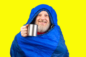 bearded man in a sleeping bag on a yellow background. equipment for recreation in tourism and travel