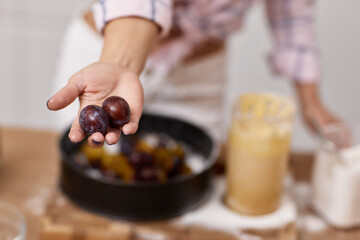 female hand showing plums for preparing plum pie in light kitchen
