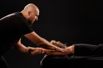 handsome male masseur giving massage to girl on black background, concept of therapeutic relaxing...