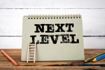 Next Level. Green notepad on wooden texture table and white background