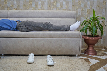 the guy is lying and resting on the sofa,boy student resting on the sofa in the living room and white sneakers near the sofa
