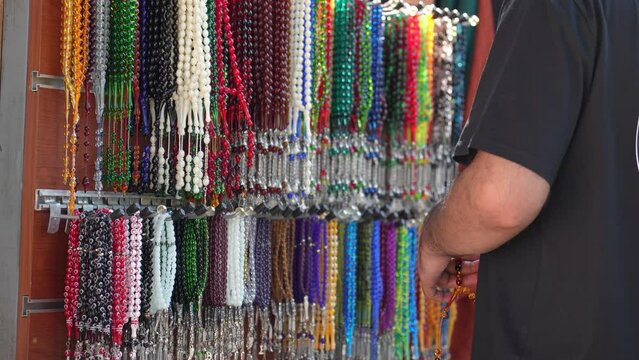 Plastic Rosary Market Overview, Buyer Hand Touching and Choosing Colorful Plastic Close-up on Market. Religious beads with colorful strings. Beautiful muslim rosary nom. Colorful chaplets for prayers.