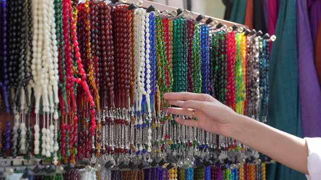 Plastic Rosary Market Overview, Buyer Hand Touching and Choosing Colorful Plastic Close-up on Market. Religious beads with colorful strings. Beautiful muslim rosary nom. Colorful chaplets for prayers.