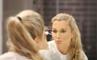 woman looking in the mirror in the bathroom and taking care of her skin.