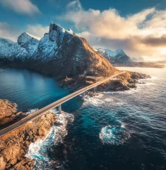 Poster Aerial view of bridge, sea with waves and mountains at sunset in Lofoten Islands, Norway. Landscape with beautiful road, water, rocks, blue sky with clouds and golden sunlight. Top view from drone © den-belitsky