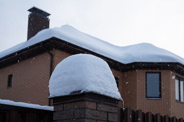 Fence and house roof under snowdrift. Heavy snowfall season
