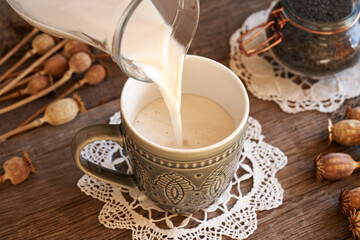 Pouring vegan poppy seed milk from a glass jug