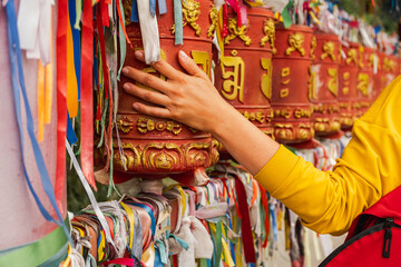 Person pilgrim female hand touching turning spinning Buddhist prayer wheel at Buddhist monastery. Prayer wheels in Buddhist stupa temple. Buddhism religion concept