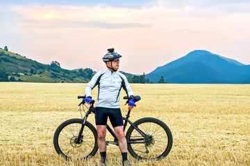 the cyclist with the bike resting on straw harvested field