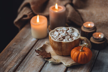 Fototapeta na wymiar Spicy sweet fall hot drink: delicious pumpkin latte with cinnamon, marshmallow with salted caramel. Served in handmade artisan mug in shape of pumpkins, cozy home decor with candles, dry autumn leaves