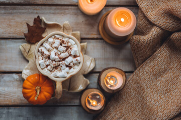Fototapeta na wymiar Flat lay top view. Spicy sweet fall hot drink: delicious pumpkin latte with cinnamon, marshmallow. Served in handmade artisan mug in shape of pumpkins, cozy home decor with candles, dry autumn leaves