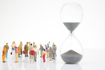 miniature people. group of different people stand near an hourglass against a white background....