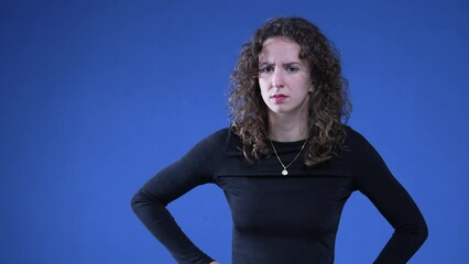 Shocked woman reacting with perplexity on blue background with hands on hip, surprised annoyed and disbelief