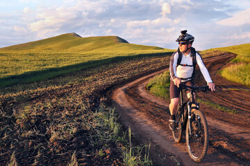 cyclist on bike rides along the fields of wheat in the sunlight
