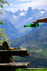 Fototapeta premium Pouring from high height of natural Asturian cider made from fermented apples, Asturian cabrales cow blue cheese with view on Naranjo de Bulnes top of Picos de Europa mountains, Spain