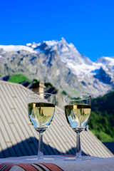 Drinking of dry white Roussette de Savoie and Vin de Savoie wine from Savoy region with view on Hautes Alpes mountains with snow on tops in summer